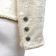 Close-up detail of engraved silver-tone Chanel CC buttons on ivory bouclé jacket cuff