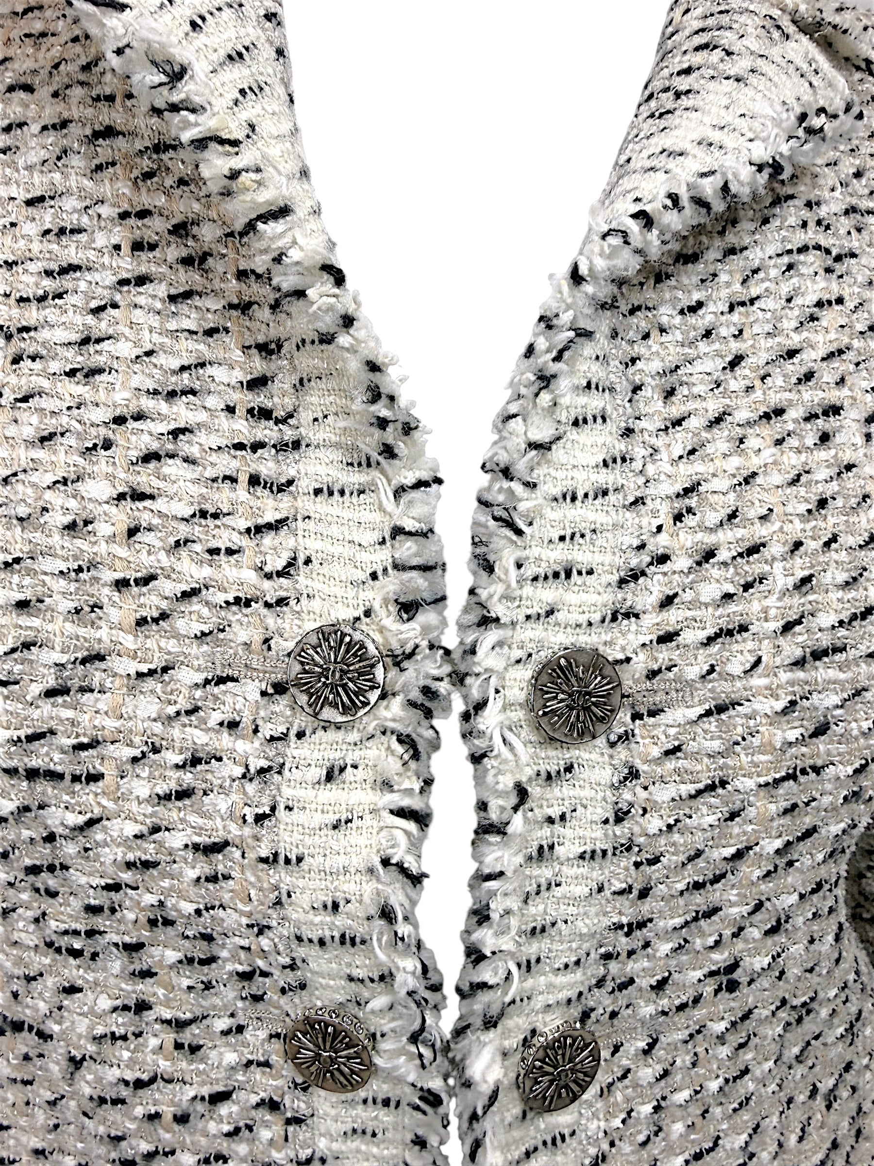 Detailed view of Chanel silver-tone logo buttons and fringe trim on ivory black Lesage tweed jacket from 2004