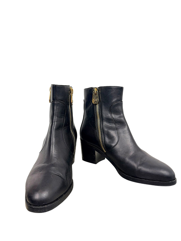 Chanel black leather double zip moto ankle boots in angled front view featuring gold-tone CC zipper hardware, rounded toes and block heels.