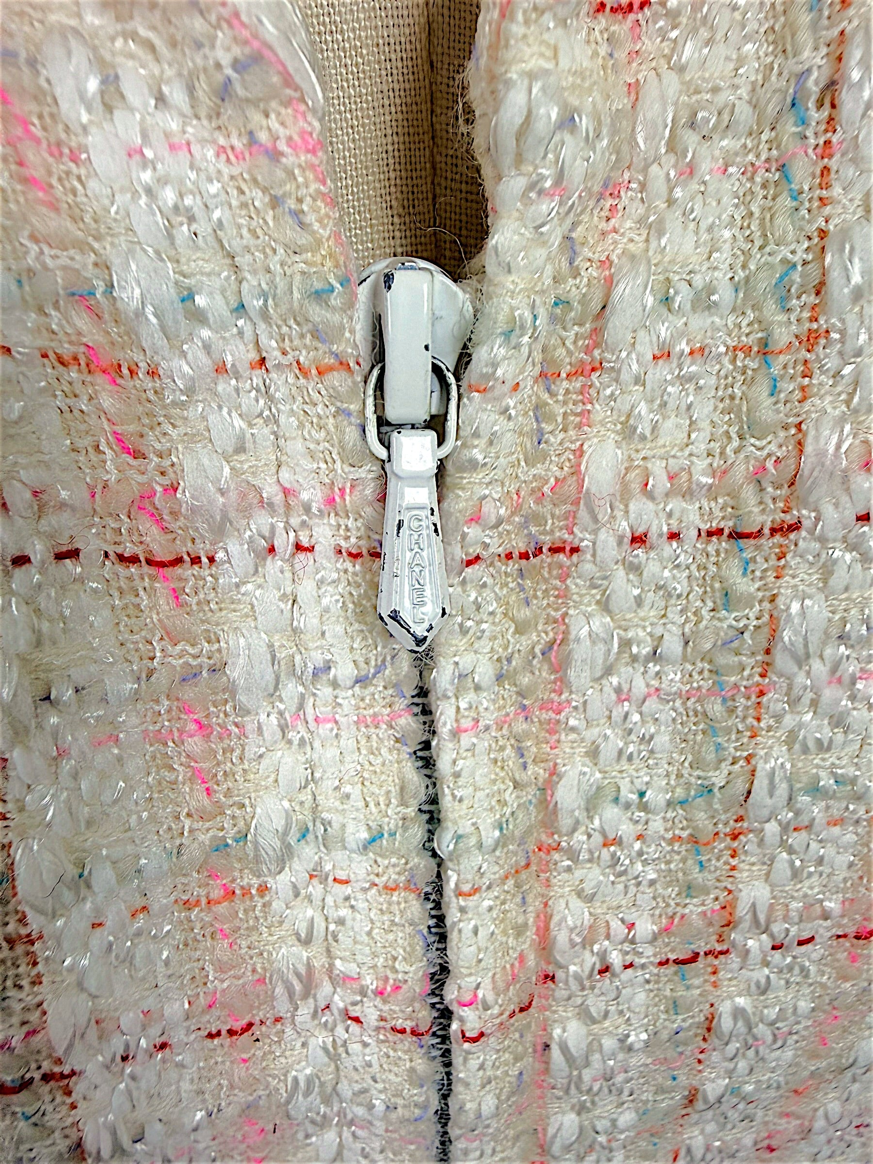 Close-up of the authentic Chanel logo zipper pull on the Cruise 2004 ivory fantasy tweed jacket, highlighting the concealed zip closure and richly textured bouclé fabric.