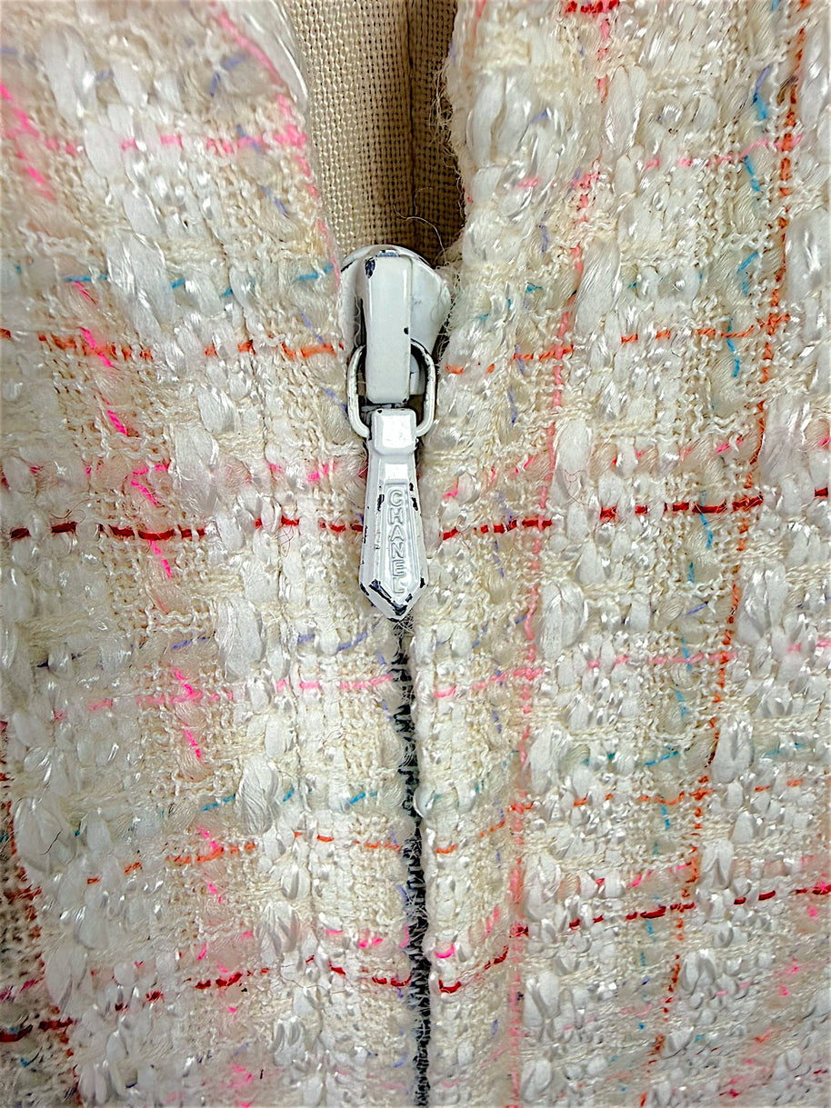 Close-up of the authentic Chanel logo zipper pull on the Cruise 2004 ivory fantasy tweed jacket, highlighting the concealed zip closure and richly textured bouclé fabric.