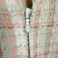 Close-up of the authentic Chanel logo zipper pull on the Cruise 2004 ivory fantasy tweed jacket, highlighting the concealed zip closure and richly textured bouclé fabric.