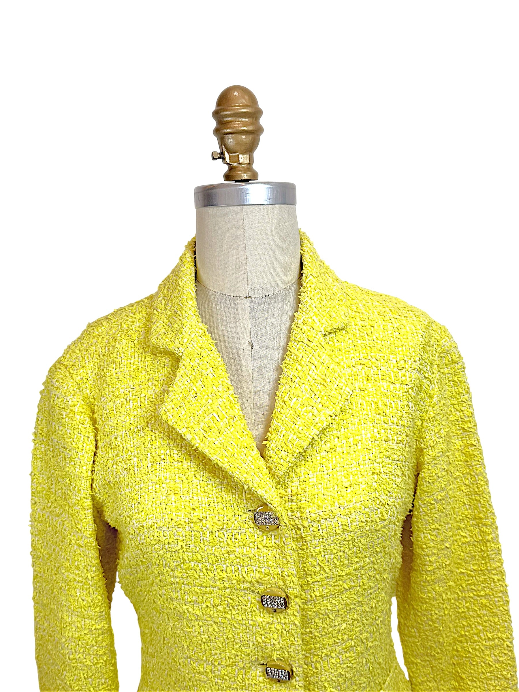 Close front upper view of Chanel Cruise 2012 yellow bouclé tweed runway jacket featuring structured lapel collar and jeweled CC buttons