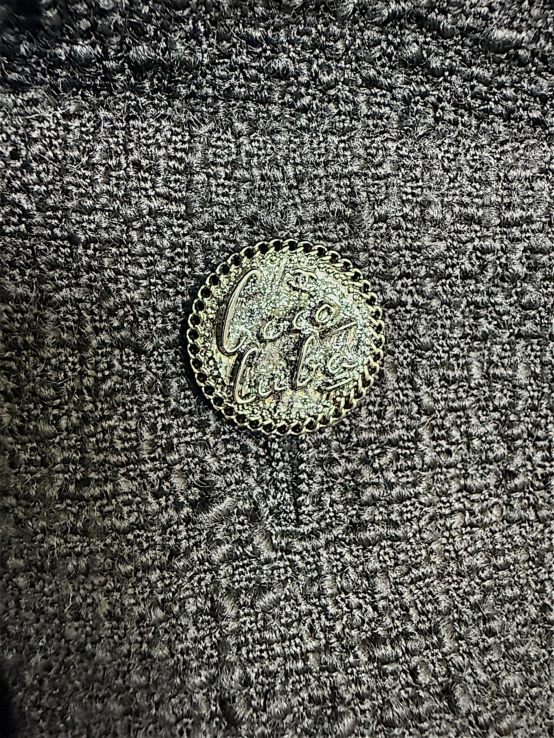 Close-up detail of the signature Chanel logo button securing the front patch pocket on the Cruise 2017 textured black jacket.