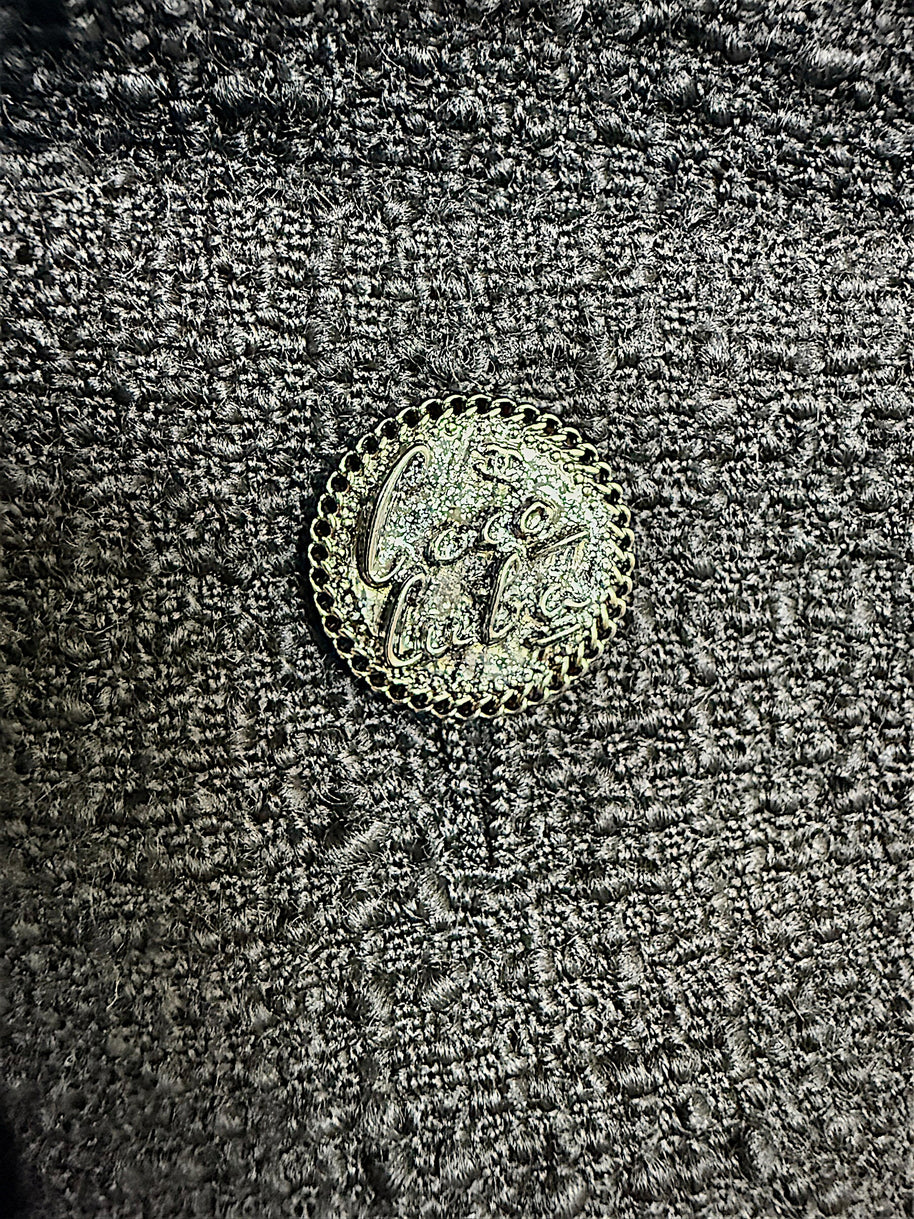 Close-up detail of the signature Chanel logo button securing the front patch pocket on the Cruise 2017 textured black jacket.