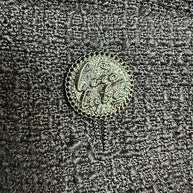 Close-up detail of the signature Chanel logo button securing the front patch pocket on the Cruise 2017 textured black jacket.