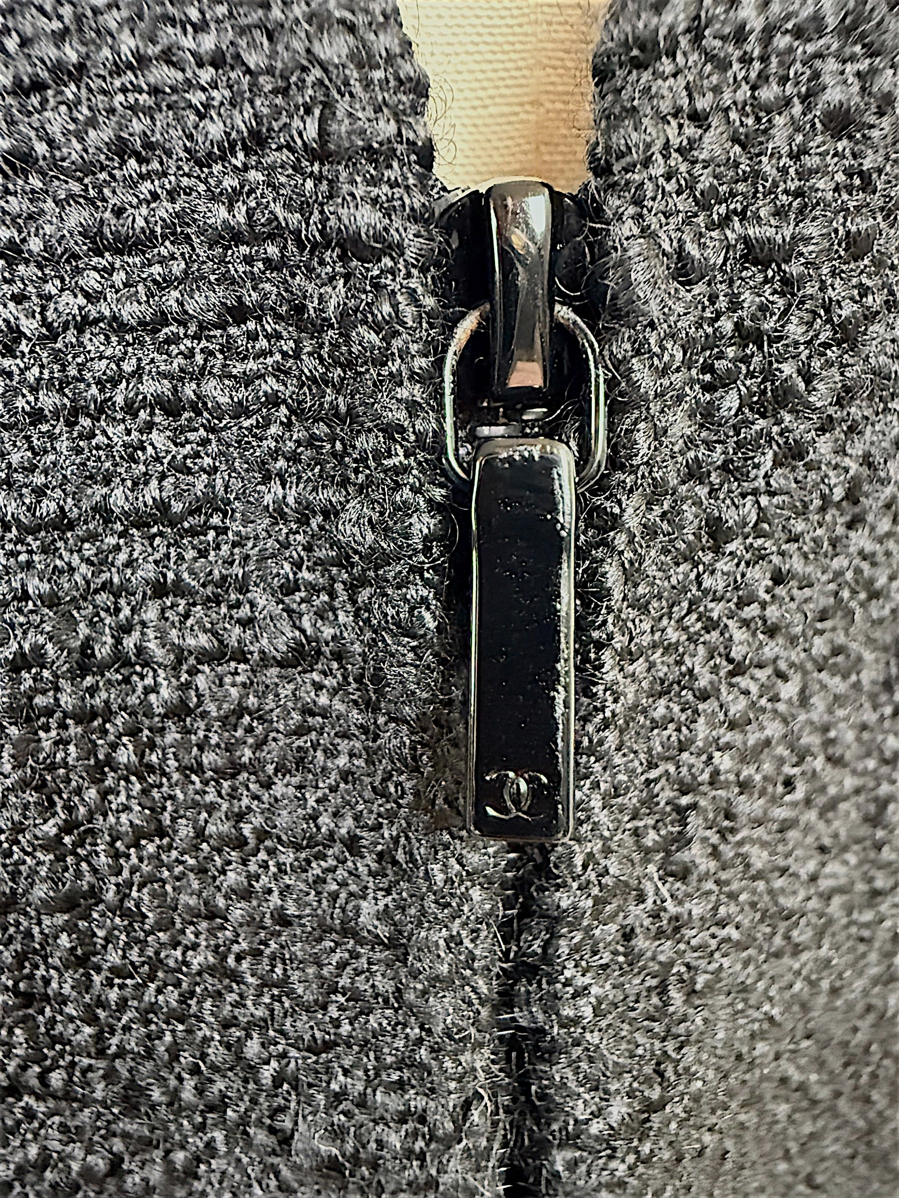 Close-up detail of the black Chanel CC logo zipper pull and textured woven fabric on the authentic Chanel Cruise 2017 (2017C) Runway Look 32 tailored jacket.