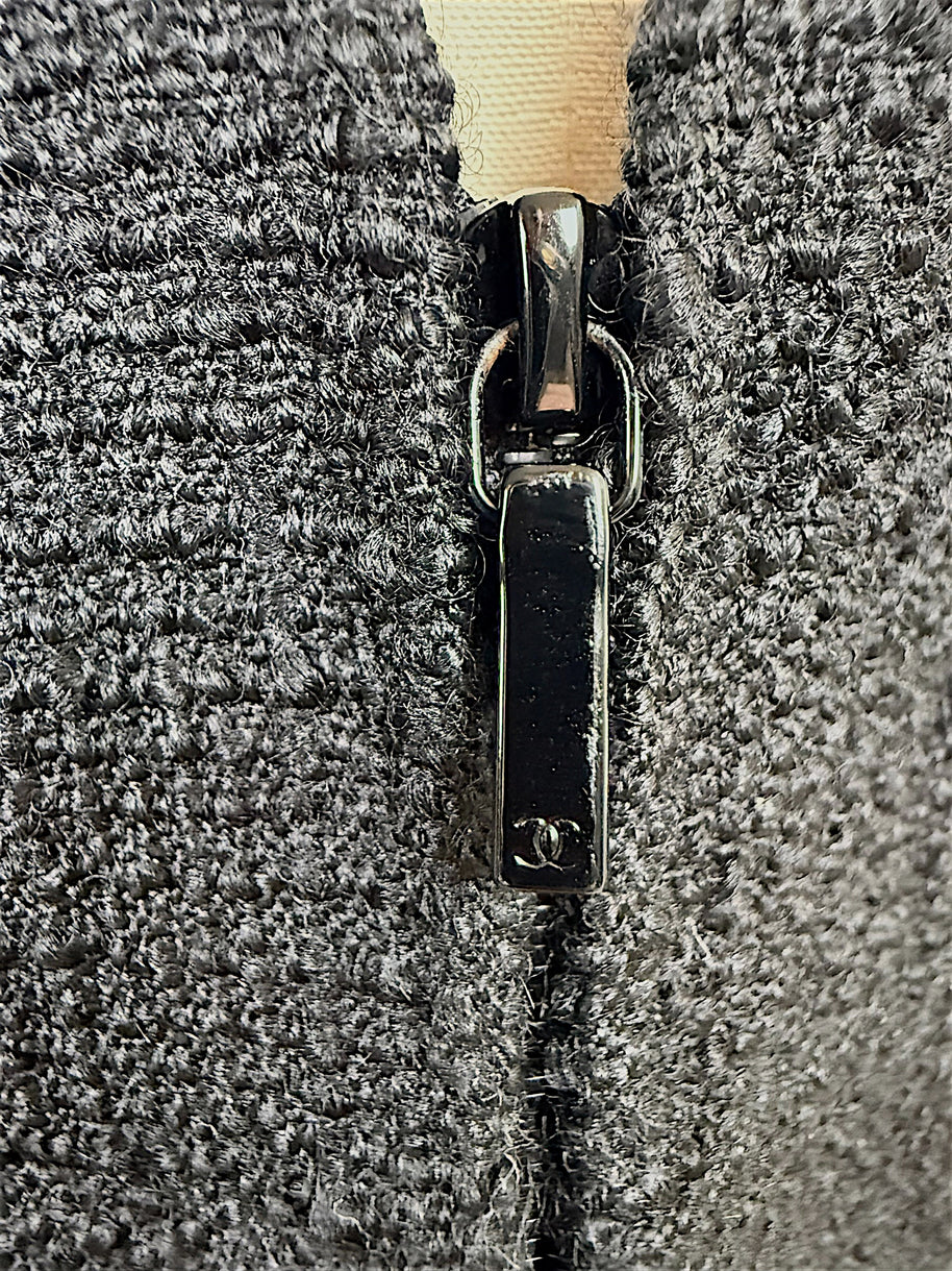 Close-up detail of the black Chanel CC logo zipper pull and textured woven fabric on the authentic Chanel Cruise 2017 (2017C) Runway Look 32 tailored jacket.