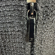 Close-up detail of the black Chanel CC logo zipper pull and textured woven fabric on the authentic Chanel Cruise 2017 (2017C) Runway Look 32 tailored jacket.