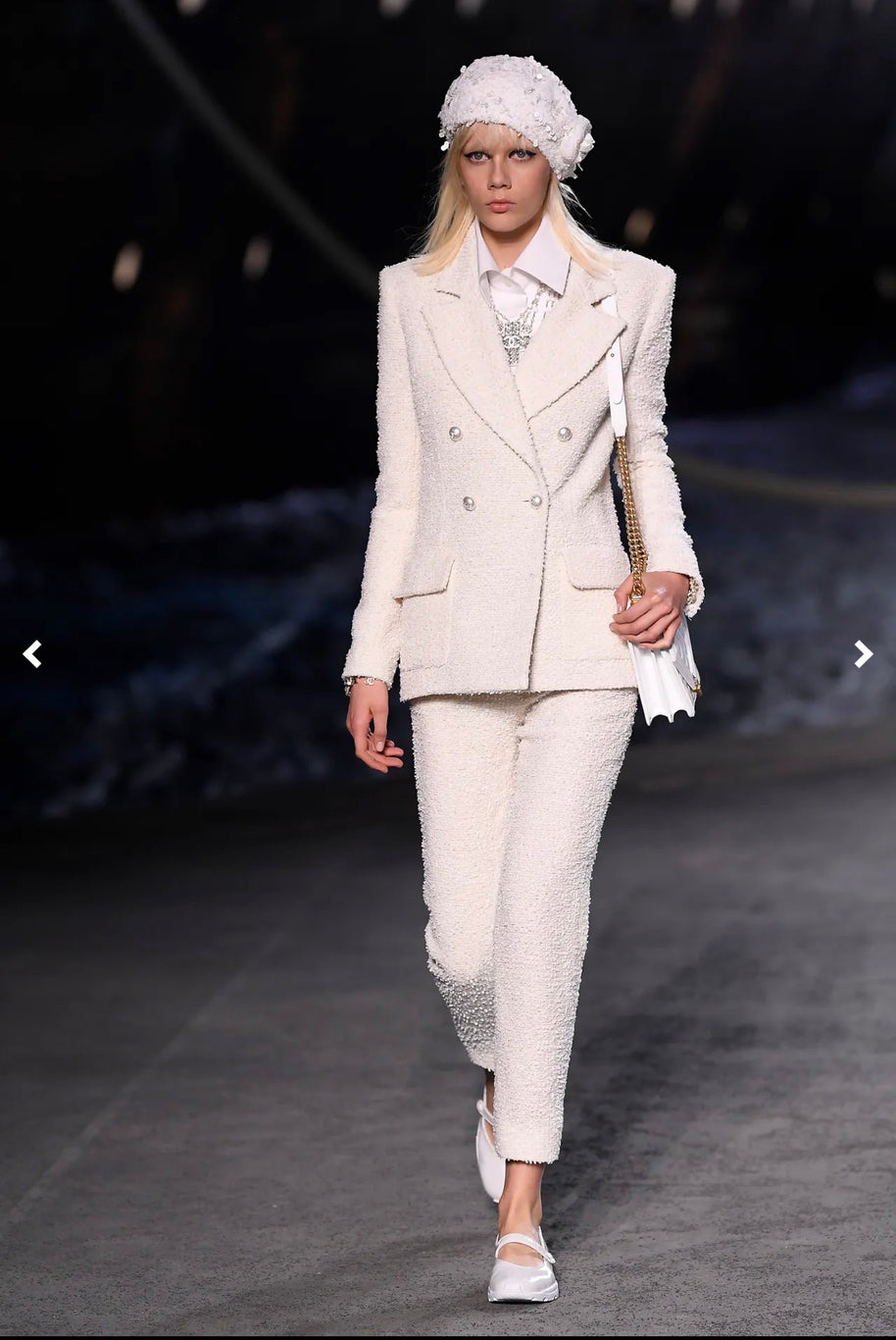 Model wearing Chanel Cruise 2019 Runway Look 26 featuring an ivory fantasy tweed double-breasted jacket designed by Karl Lagerfeld with coordinating trousers and white accessories.