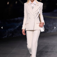 Model wearing Chanel Cruise 2019 Runway Look 26 featuring an ivory fantasy tweed double-breasted jacket designed by Karl Lagerfeld with coordinating trousers and white accessories.