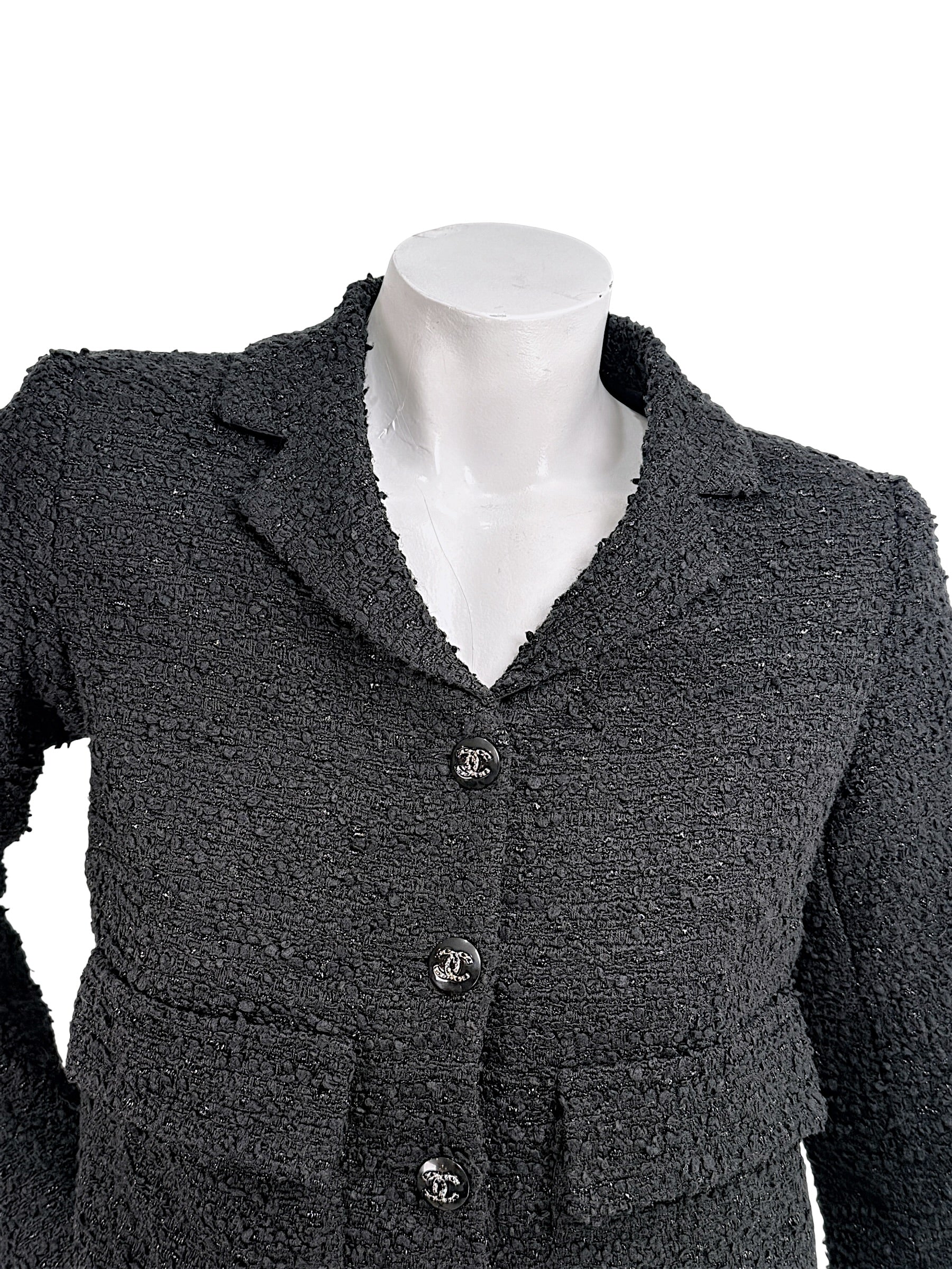 Close-up of Chanel Cruise 2021 black bouclé tweed jacket showing textured fabrication and signature CC logo buttons