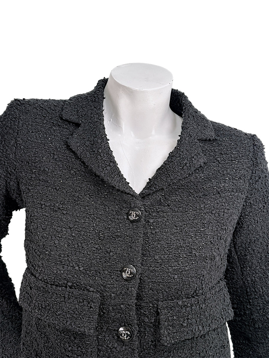 Close-up of Chanel Cruise 2021 black bouclé tweed jacket showing textured fabrication and signature CC logo buttons