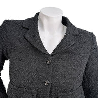 Close-up of Chanel Cruise 2021 black bouclé tweed jacket showing textured fabrication and signature CC logo buttons