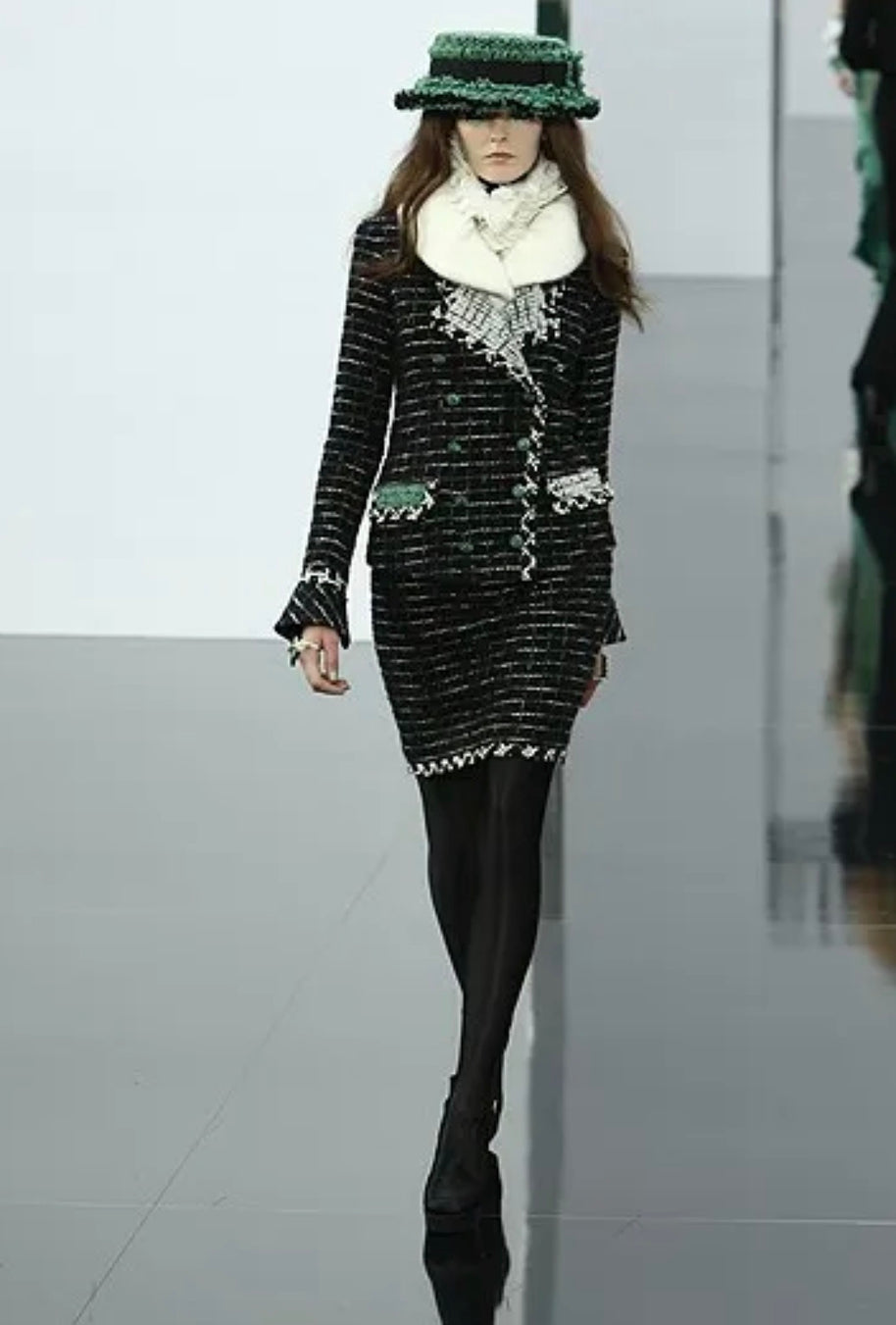 Documented Chanel Fall 2009 Runway Look 22 as presented on the runway under Karl Lagerfeld, featuring the original styling with oversized emerald tweed hat, ivory fur collar, and matching black bouclé tweed skirt suit.