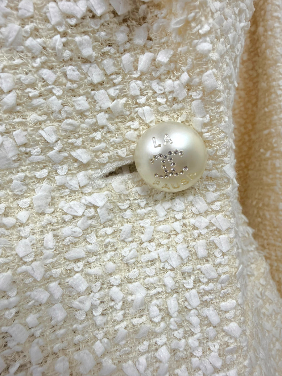Detailed view of the original Chanel pearl-effect La Pausa CC button on the ivory fantasy tweed jacket from the Cruise 2019 Runway Look 26 collection.