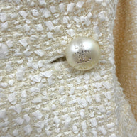 Detailed view of the original Chanel pearl-effect La Pausa CC button on the ivory fantasy tweed jacket from the Cruise 2019 Runway Look 26 collection.