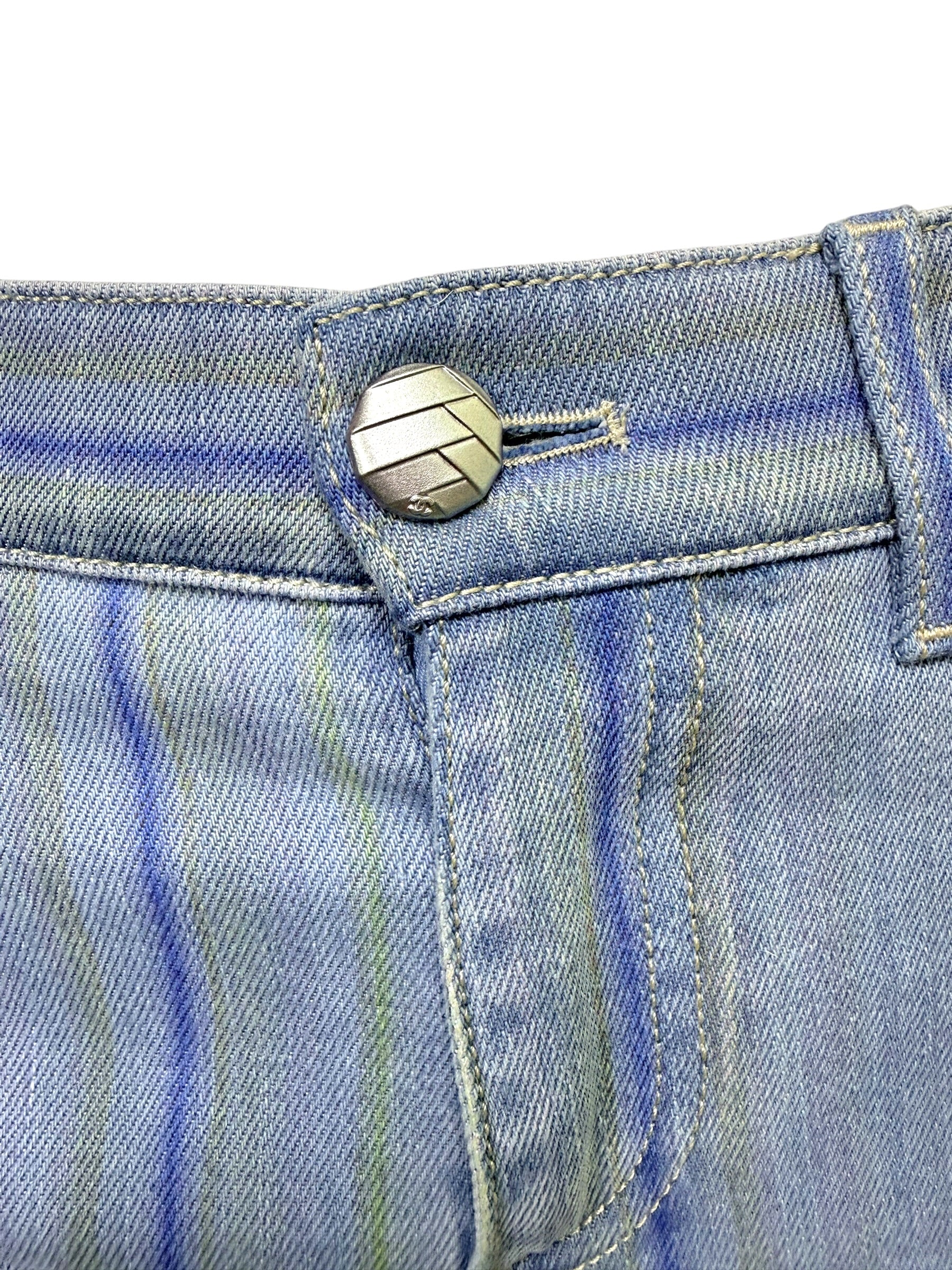 Close-up of Chanel engraved silver logo button on pale blue striped denim jeans from Spring 2006 collection.
