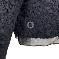Close-up of Chanel Paris button detail on black ruched textured bolero jacket
