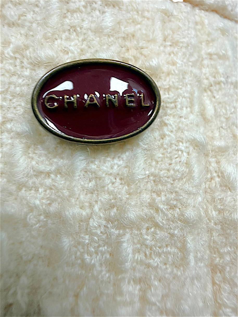 Close-up of the burgundy Chanel logo plaque affixed to the waistband of the ivory bouclé pencil skirt.