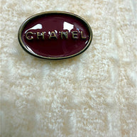 Close-up of the burgundy Chanel logo plaque affixed to the waistband of the ivory bouclé pencil skirt.