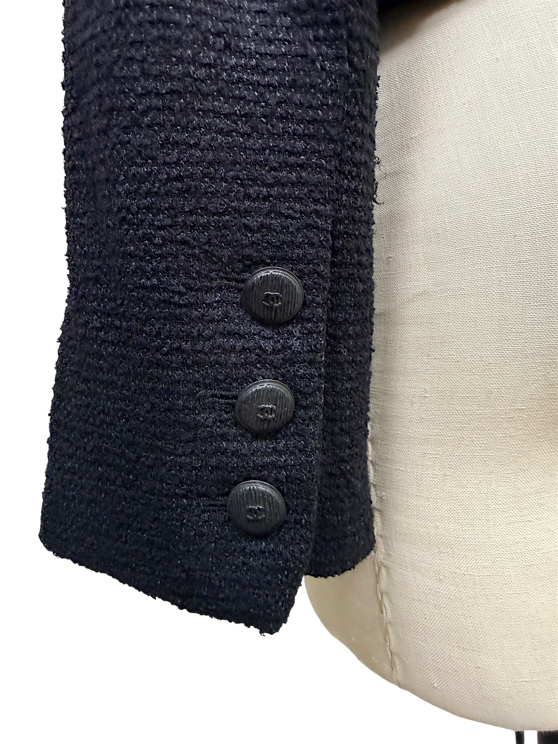 Close-up of engraved Chanel CC buttons at the sleeve cuff of the Spring Summer 2005 runway bouclé tuxedo jacket.