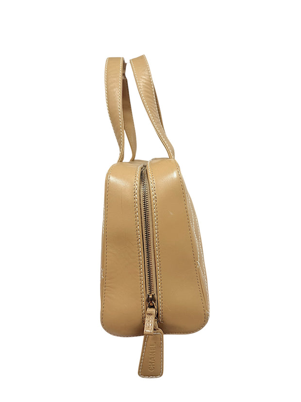 Side profile of vintage Chanel Surpique Bowler bag in beige quilted lambskin featuring top zip closure and rolled leather handles.