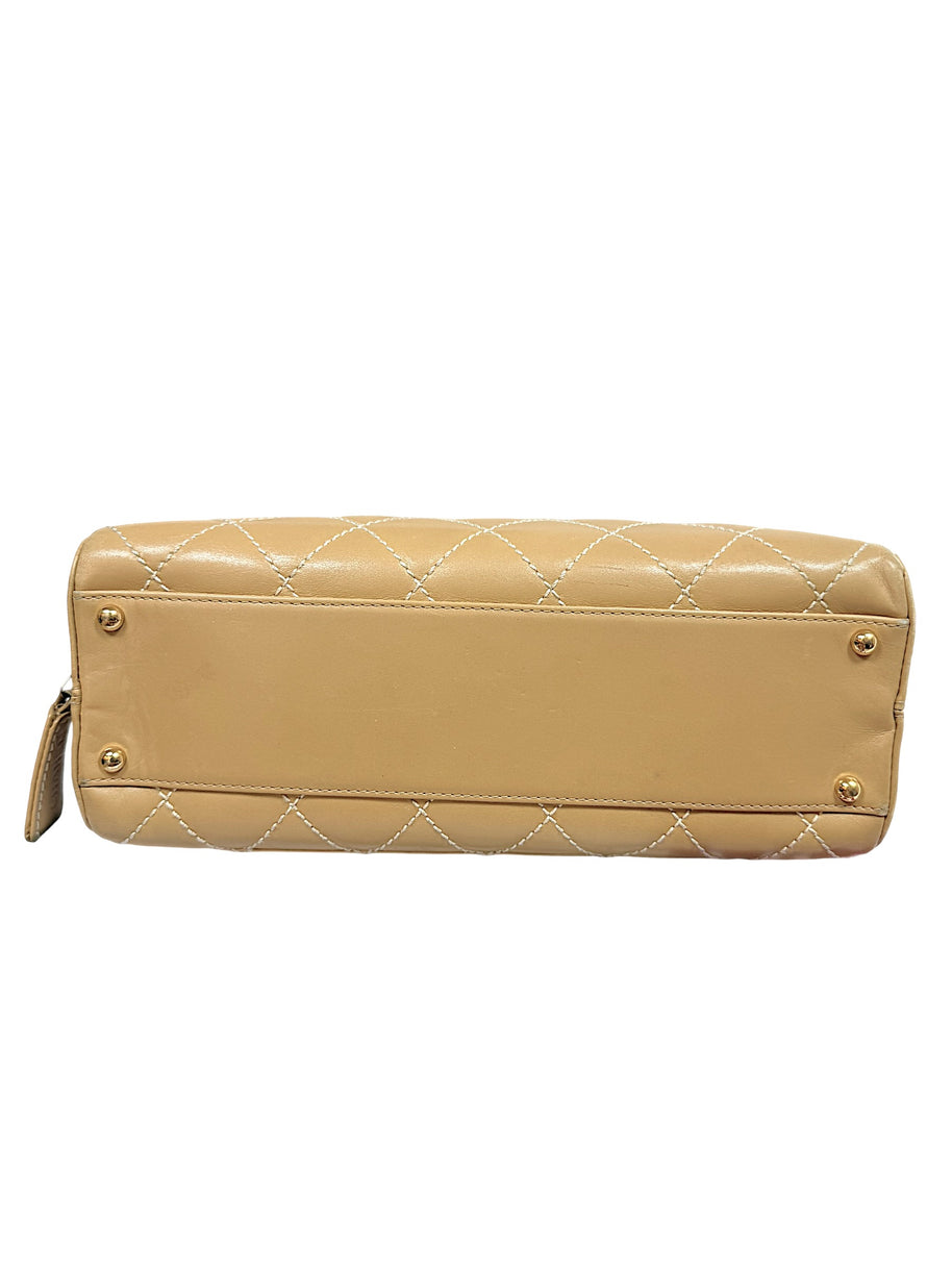 Bottom base of Chanel Surpique Bowler bag with protective gold feet and beige lambskin leather construction.