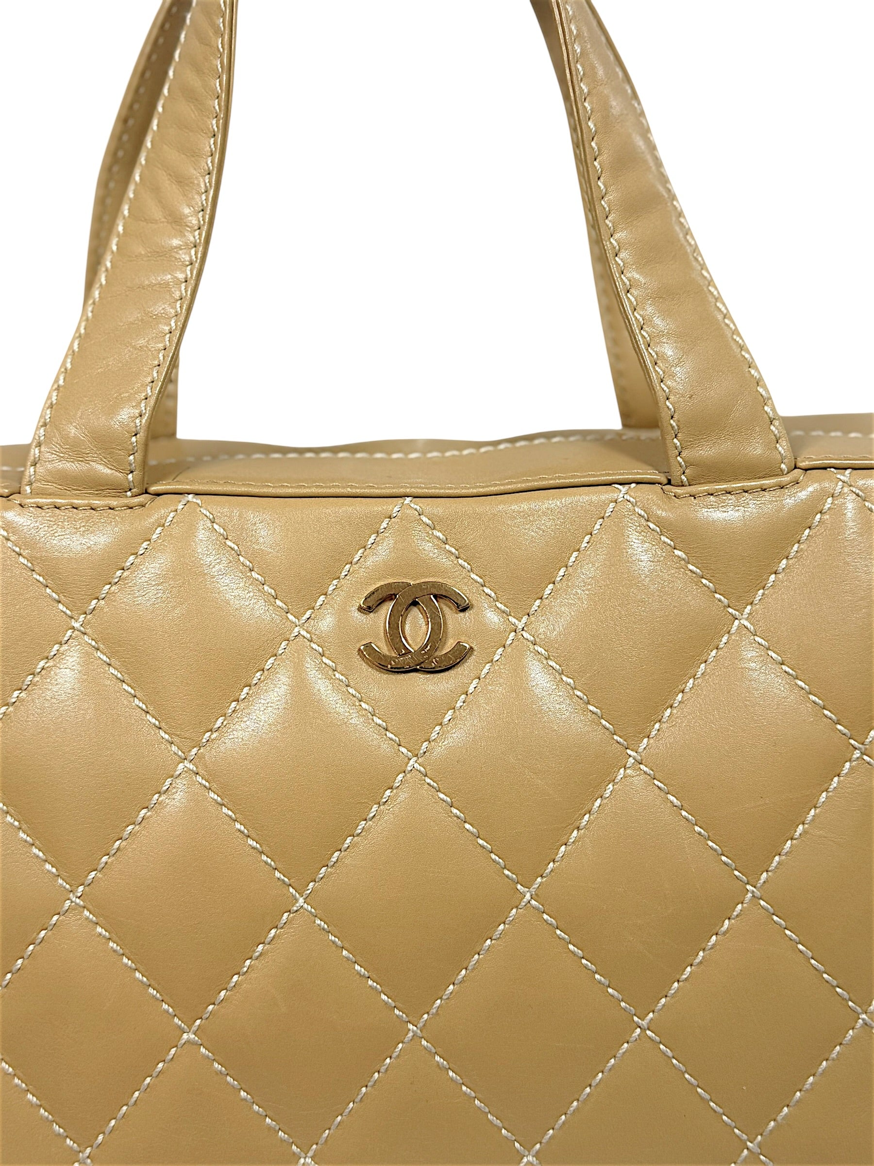 Close-up front detail of vintage Chanel Surpique Bowler bag featuring gold-tone CC logo hardware, oversized diamond quilting and beige lambskin leather.