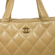 Close-up front detail of vintage Chanel Surpique Bowler bag featuring gold-tone CC logo hardware, oversized diamond quilting and beige lambskin leather.