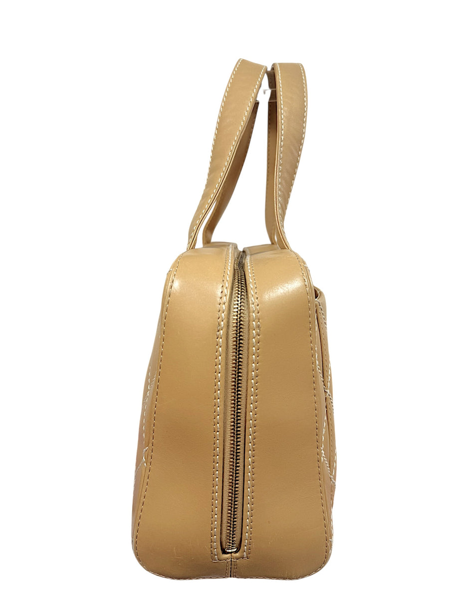 Angled side profile of Chanel vintage Surpique Bowler bag in beige quilted lambskin leather.
