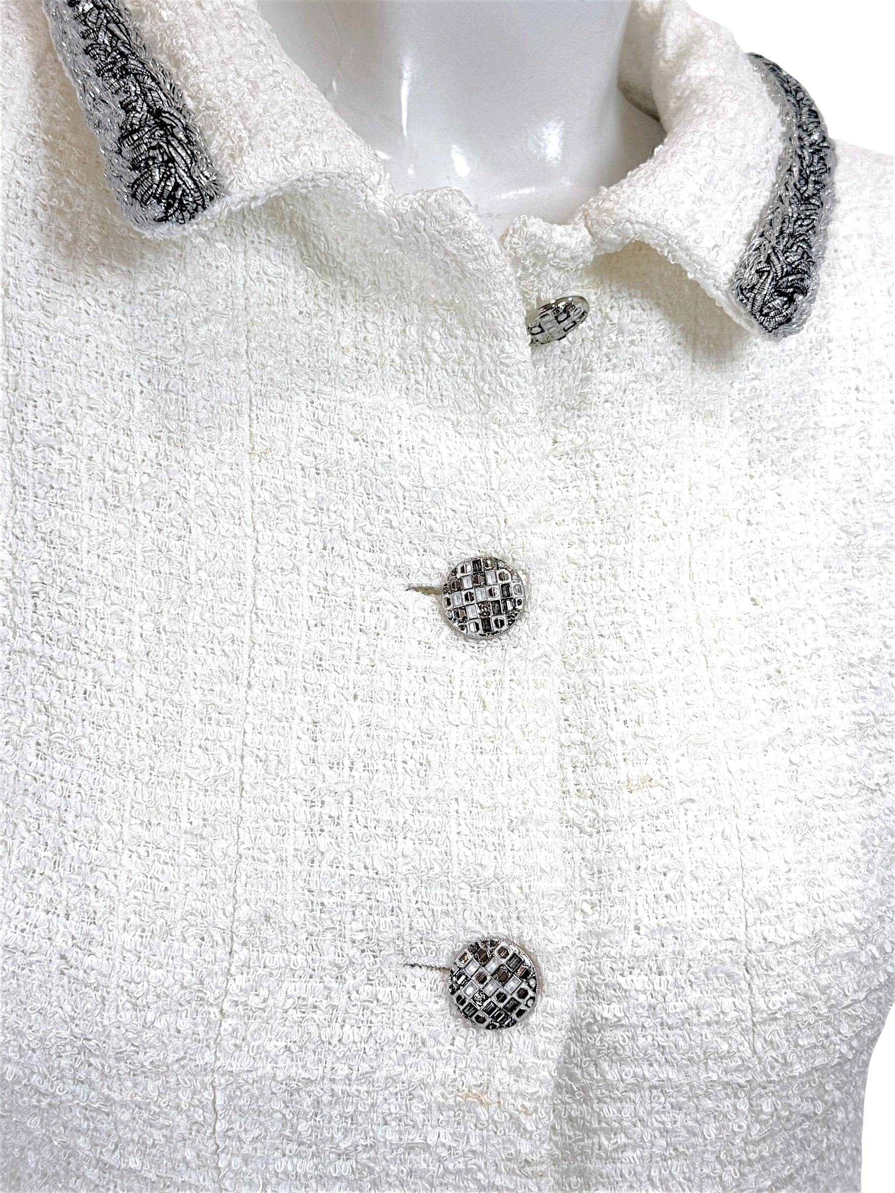 Close-up of Chanel white bouclé tweed dress featuring signature logo buttons and metallic trim collar detail