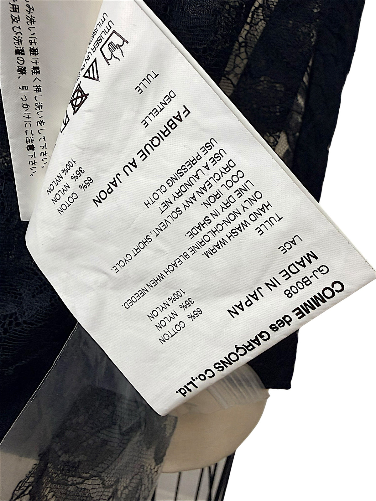 Close-up of Comme des Garçons black sheer floral lace shirt fabric composition and care label, showing 65% cotton, 35% nylon, Made in Japan and style GJ-B008.
