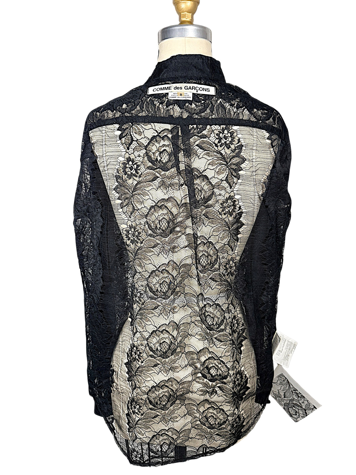 Back of Comme des Garçons black sheer floral lace shirt on dress form, showing floral pattern, collar and original designer label.