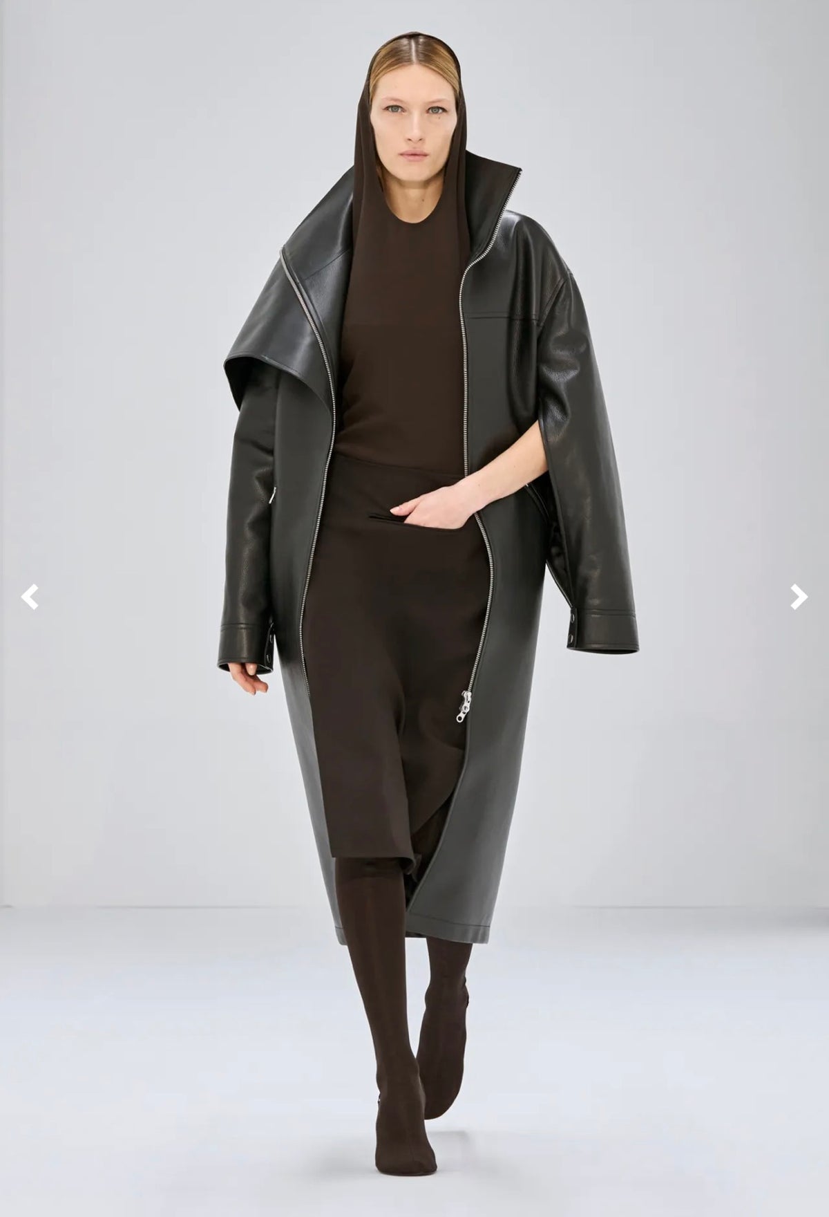 Courrèges Fall 2024 Ready-to-Wear Look 23 runway model wearing the Oblique Space hooded dress layered beneath an oversized black leather coat.