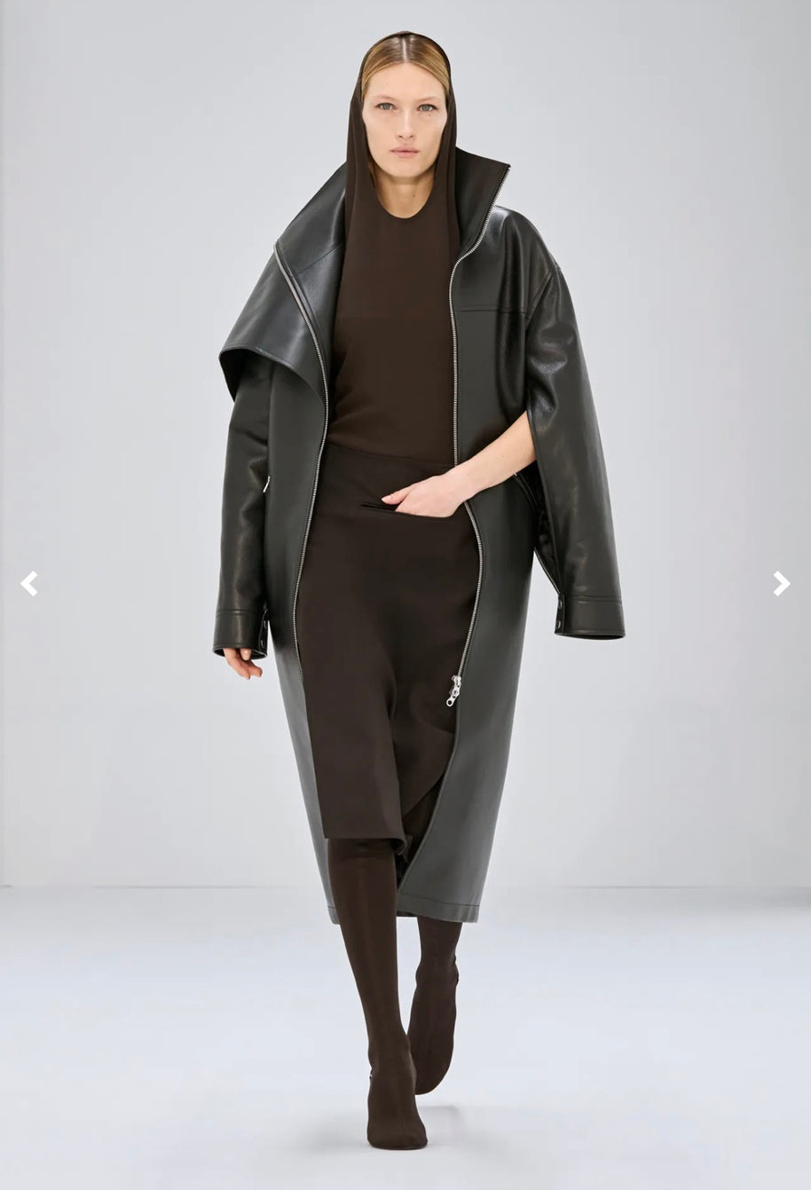 Courrèges Fall 2024 Ready-to-Wear Look 23 runway model wearing the Oblique Space hooded dress layered beneath an oversized black leather coat.