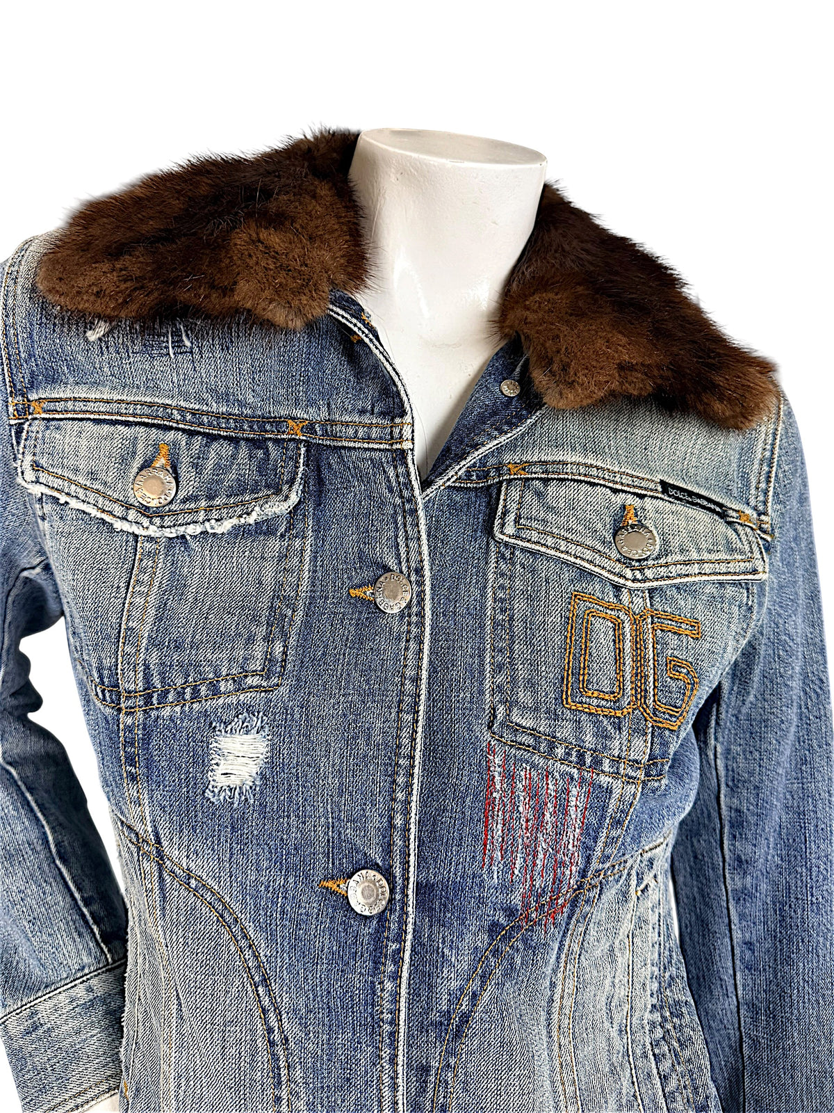 Close-up of Dolce & Gabbana vintage denim jacket showing brown fur collar, flap chest pockets, silver-tone logo buttons, and embroidered 05 detail.