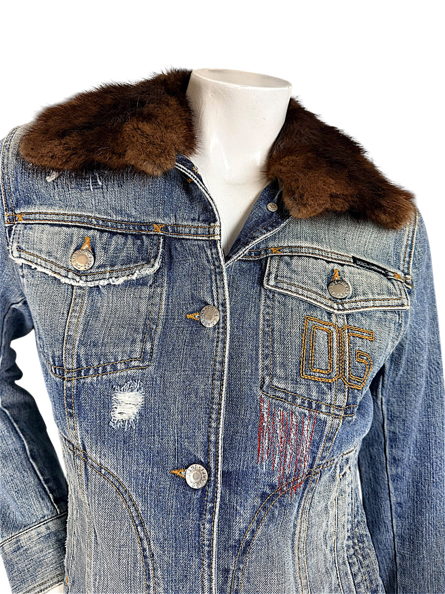 Close-up of Dolce & Gabbana vintage denim jacket showing brown fur collar, flap chest pockets, silver-tone logo buttons, and embroidered 05 detail.