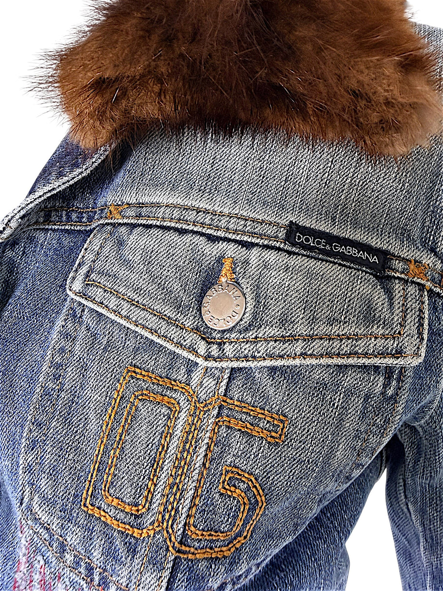 Close-up of vintage Dolce & Gabbana denim jacket with golden-brown embroidered 05 motif, black designer label, branded pocket button, and fur collar.