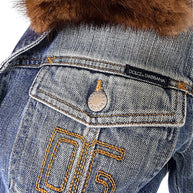 Close-up of vintage Dolce & Gabbana denim jacket with golden-brown embroidered 05 motif, black designer label, branded pocket button, and fur collar.