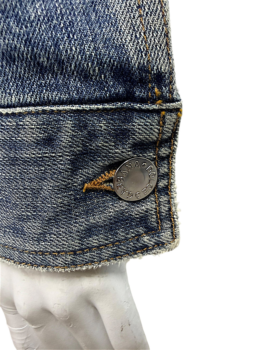 Macro detail of silver-tone Dolce & Gabbana engraved metal button on vintage distressed blue cotton denim jacket with contrast golden stitching.