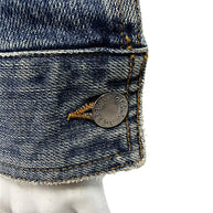 Macro detail of silver-tone Dolce & Gabbana engraved metal button on vintage distressed blue cotton denim jacket with contrast golden stitching.