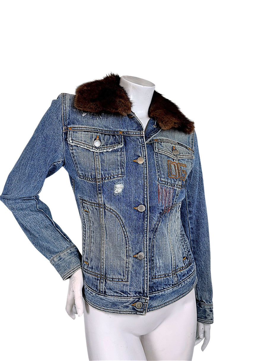 Three-quarter front view of Dolce & Gabbana vintage blue denim jacket highlighting its fitted waist, brown fur collar, distressed finish, and embroidered chest.