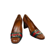 Authentic Gucci brown pebbled leather block heel pumps with signature green and red Web stripe and oversized interlocking GG hardware, angled front view.