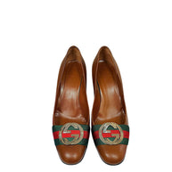 Front view of authentic Gucci brown leather pumps featuring green and red Web stripe detail and polished interlocking GG logo hardware.