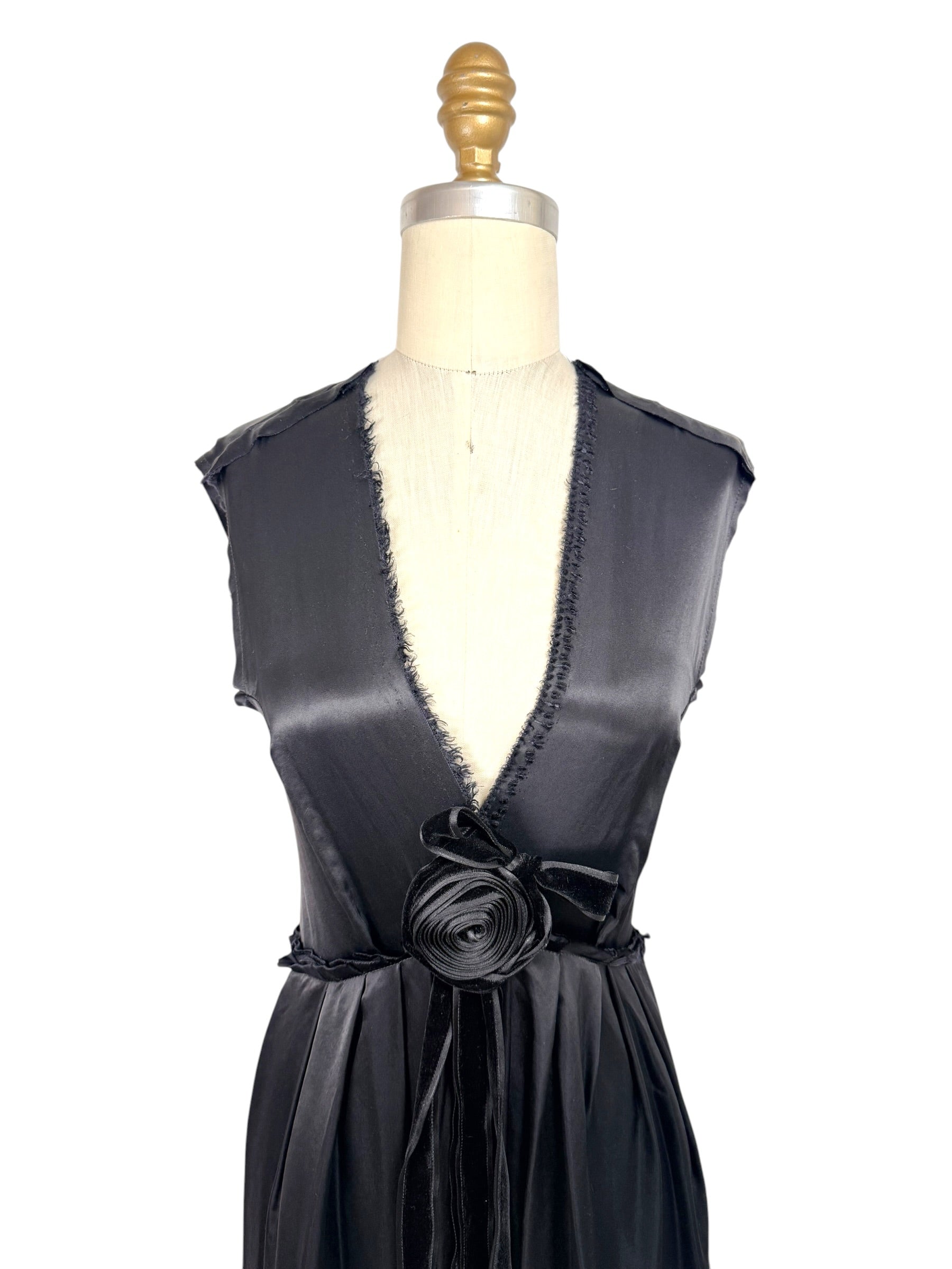 Close front detail of Lanvin Hiver 2005 black satin dress showing deep plunge neckline with frayed trim and sculptural satin rosette accent.