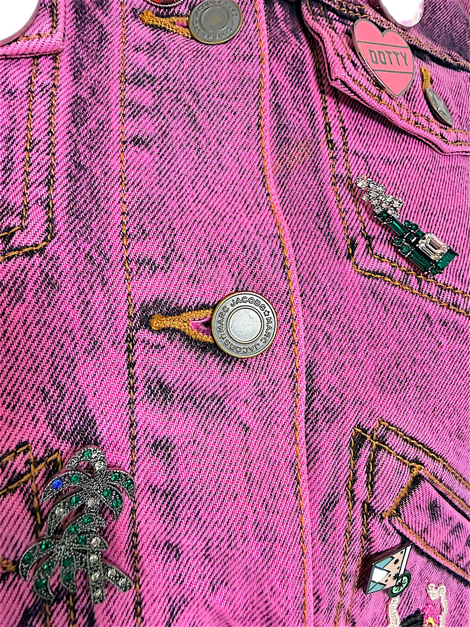 Detailed view of Marc Jacobs engraved metal buttons, pink DOTTY heart pin, palm tree embellishment and acid wash denim stitching.
