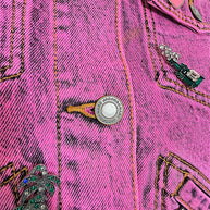 Detailed view of Marc Jacobs engraved metal buttons, pink DOTTY heart pin, palm tree embellishment and acid wash denim stitching.