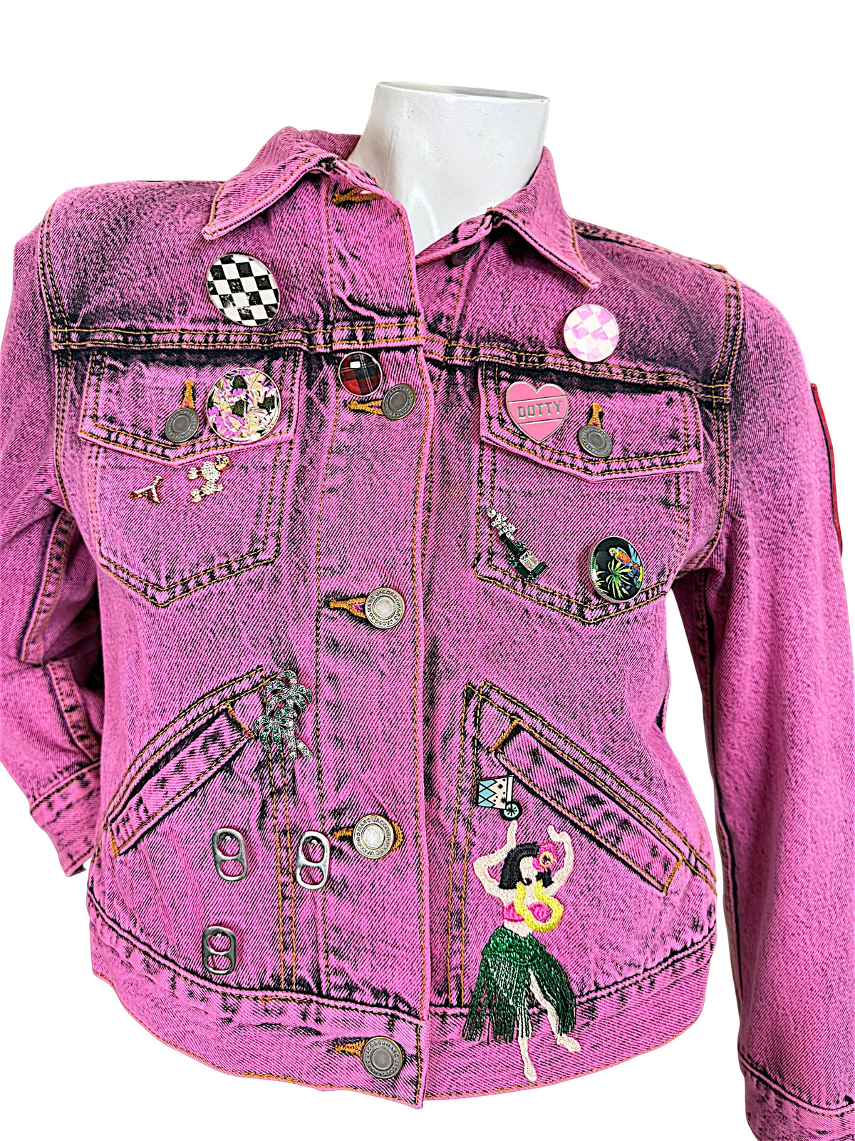 Close-up of Marc Jacobs pink acid wash denim jacket featuring checkerboard pins, embroidered palm trees, hula dancer and branded metal buttons.
