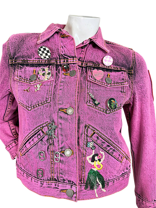 Close-up of Marc Jacobs pink acid wash denim jacket featuring checkerboard pins, embroidered palm trees, hula dancer and branded metal buttons.